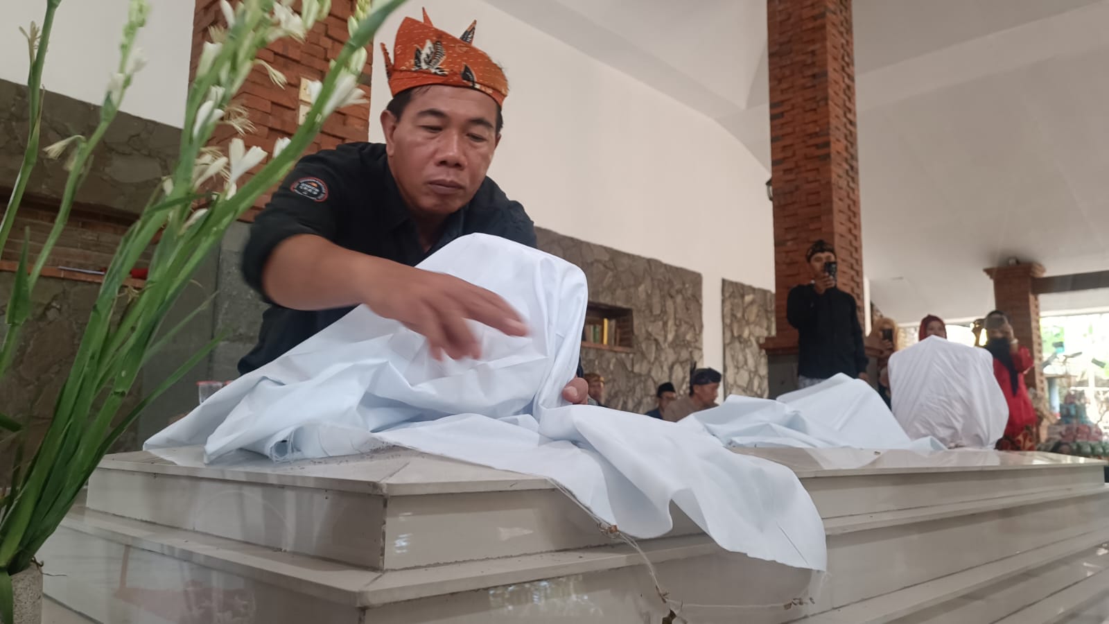Tokoh masyarakat Desa Prasung, Bahrul Amig tengah mengganti kain kafan pembungkus nisan makam Mbah Sholeh, Minggu (13/7/2025). (Foto : Eleanor)